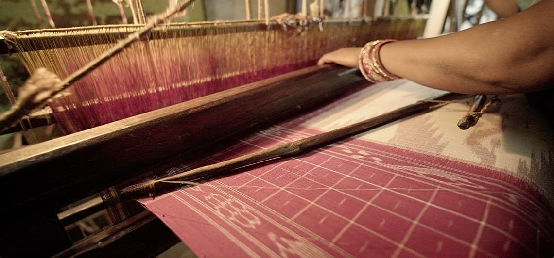 A weaver's hands guiding a Sambalpuri Bandha ikat pattern on the handloom